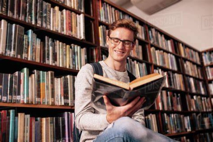 Young caucasian man reading book while sitting in college library